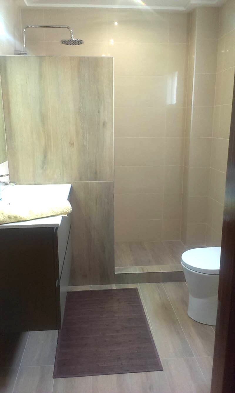 Baño con ducha a ras de suelo, mampara de cristal y mueble de madera