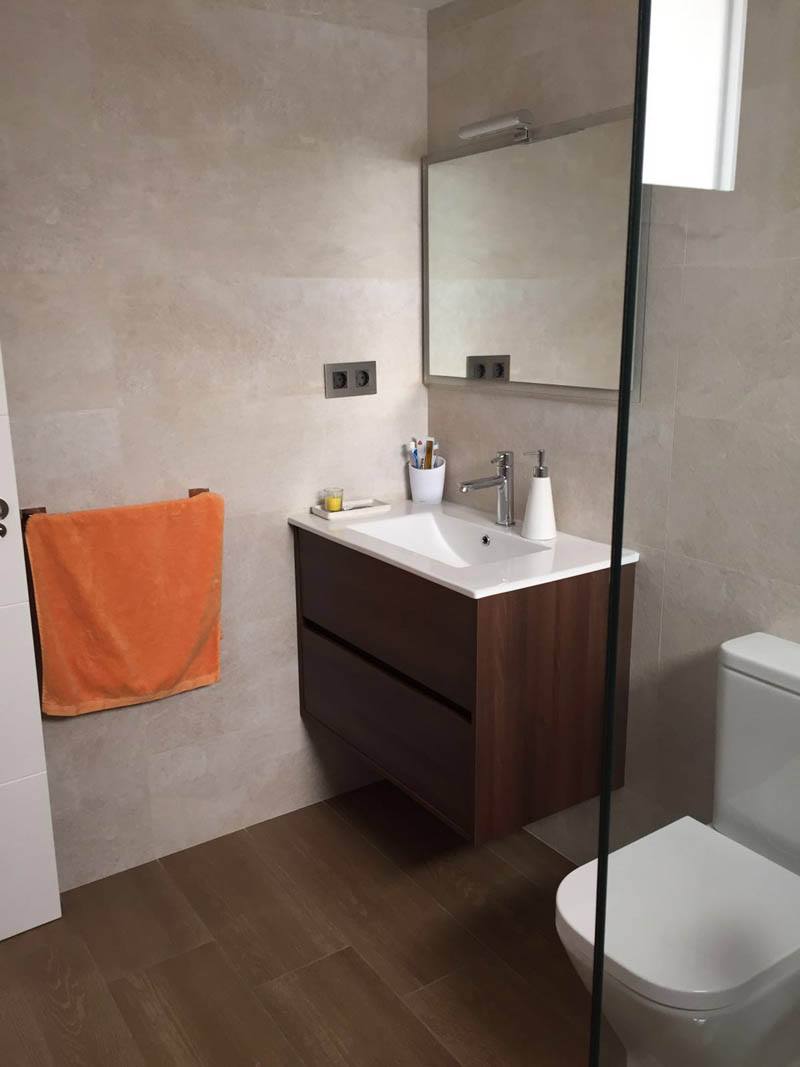 Baño moderno con mueble suspendido en madera oscura y grifería cromada